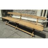 A vintage long wooden bench with slatted seat and back rail raised on x framed supports united by