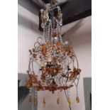 An open scrolling light metal hanging ceiling light with floral detail, trailing prism swags and