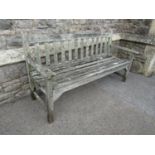 A weathered teak three seat garden bench with slatted seat and back, probably a Lister example,