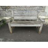 A Swan Hattersley weathered teak two seat garden bench with slatted seat and back beneath a curved