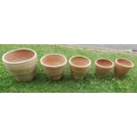 A graduated set of contemporary terracotta planters of circular tapered form with simple incised