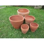 A graduated set of terracotta planters of circular tapered form with simple incised bands, the