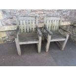 A pair of weathered heavy gauge teak garden open armchairs with slatted seats and backs, labelled