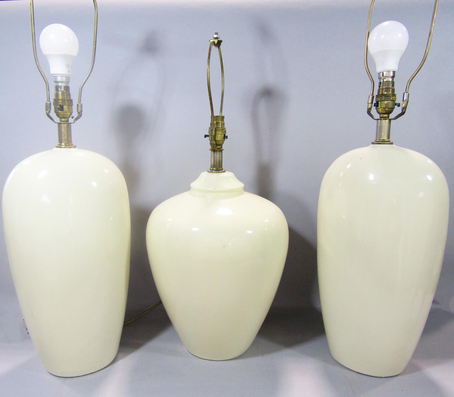 A pair of cream glazed table lamps and a single similar lamp, all 73cm high