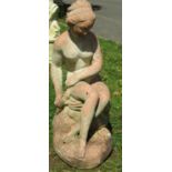 A weathered cast composition stone garden ornament in the form of a seated classical female nude,
