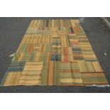 A flat weave rug with striped patchwork panels, in multicoloured tones on a black cotton backing,