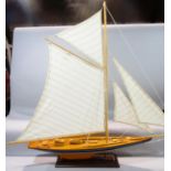 A wooden model of an early 20th century yacht, in full sail, raised on a wooden plinth, 100m x