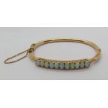 Antique 15ct opal hinged bangle set with eleven oval cabochon opals, 9.7g