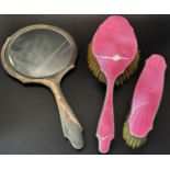 A pink enamelled hand mirror, hair brush and clothes brush with silver edging, a single silver