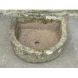 A weathered carved natural stone D shaped trough with central circular drainage hole, 57 cm wide x