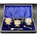 A boxed three piece silver condiment set lacks glass liners and one spoon, a silver cigarette box