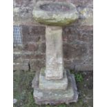 A weathered rough hewn natural stone bird bath, with square tapered pedestal and stepped base (