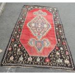 A flat weave Kilim rug with extended hooked lozenge medallion on a red ground, with a running flower