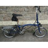 A Brompton Folding cycle in blue, with stand and cloth cover