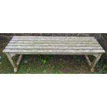 A weathered teak garden bench with rectangular open slatted seat, raised on square cut supports