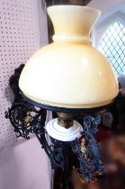 A cast iron wall bracket oil lamp, with a scrolled hinged arm with gold putti detail, shade diam