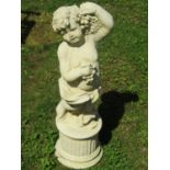 A buff coloured cast composition stone garden ornament in the form of a standing cherub clutching
