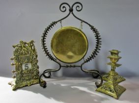 A brass dinner gong suspended in a wrought iron wire work frame, a brass Victorian desk calendar