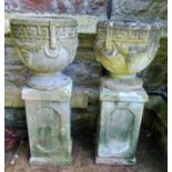 A pair of weathered cast composition stone circular garden urns with classical Greek key and fixed