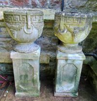 A pair of weathered cast composition stone circular garden urns with classical Greek key and fixed