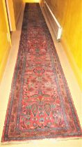 A very long eastern wool runner with repeating floral detail upon a salmon pink ground within narrow