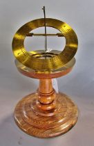 A small contemporary desk top brass sun dial on a turned wooden base, labelled to underside 'by John