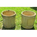 A pair of weathered cast composition stone cylindrical planters with repeating panels and stamped to