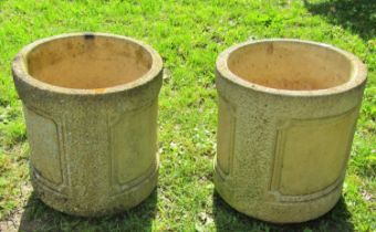 A pair of weathered cast composition stone cylindrical planters with repeating panels and stamped to