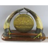 A small Victorian brass dinner gong suspended from cow horn tips raised on an oak plinth complete