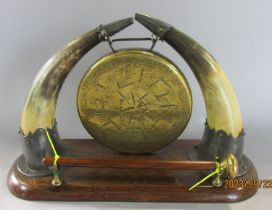 A small Victorian brass dinner gong suspended from cow horn tips raised on an oak plinth complete