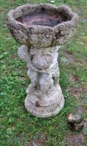A small weathered cast composition stone bird bath in the form of three cherubs supporting a
