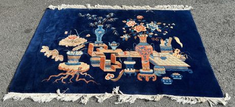 A Chinese deep pile wool carpet with an interior scene of flowers in vases on a dark blue ground,