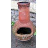 A small weathered clay chimenea raised on a simple iron stand, 61cm high