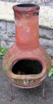 A small weathered clay chimenea raised on a simple iron stand, 61cm high