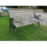 A two seat garden bench with weathered slatted seat raised on decorative pierced cast iron end