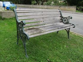 A two seat garden bench with weathered slatted seat raised on decorative pierced cast iron end