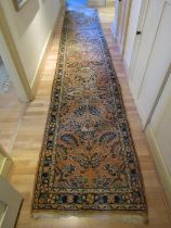 An eastern wool runner with salmon pink ground, repeating floral detail and set within running