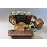 An Agfa Isolette folding camera with a brown leather case, strap and lens shade