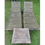 A pair of weathered teak portable garden loungers with slatted seats and adjustable head rests,