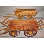 Two similar wooden models of rustic hay carts, one a single horse drawn cart, the other a two