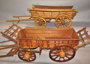 Two similar wooden models of rustic hay carts, one a single horse drawn cart, the other a two