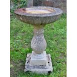 A weathered cast composition stone two section bird bath with circular top raised on a baluster