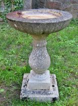 A weathered cast composition stone two section bird bath with circular top raised on a baluster