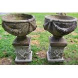 A pair of weathered cast composition stone garden urns, the circular bowls with repeating