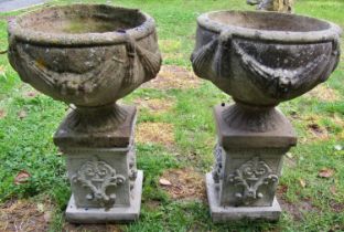 A pair of weathered cast composition stone garden urns, the circular bowls with repeating
