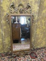 An antique gilded pier glass, with shaped outline and floral scrolling detail, 110cm high x 55cm