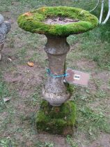A weathered composition stone bird bath of circular form raised on a fixed baluster shaped