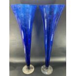 A pair of large blue flared trumpet vases with a clear circular foot, both standing one metre tall