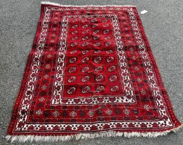 A small Afghan style red ground rug with a panel of four rows of guls on a red ground, worn in