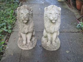 A pair of weathered cast composition stone garden/pier ornaments in the form of seated lions with